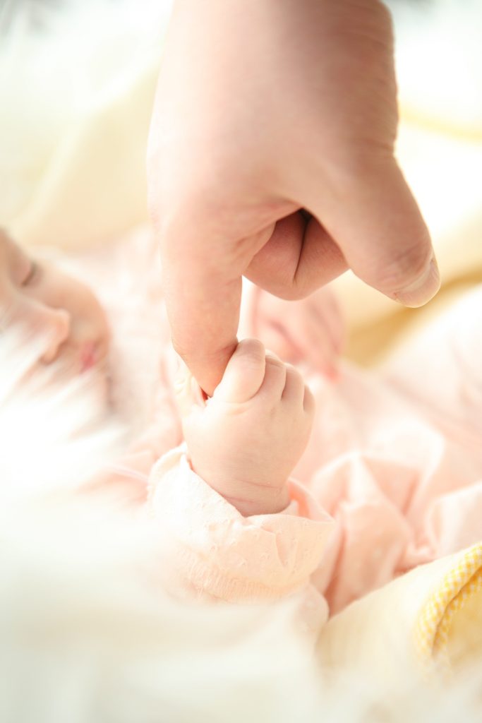 A newborn baby grasps an adult's finger with their small hand.